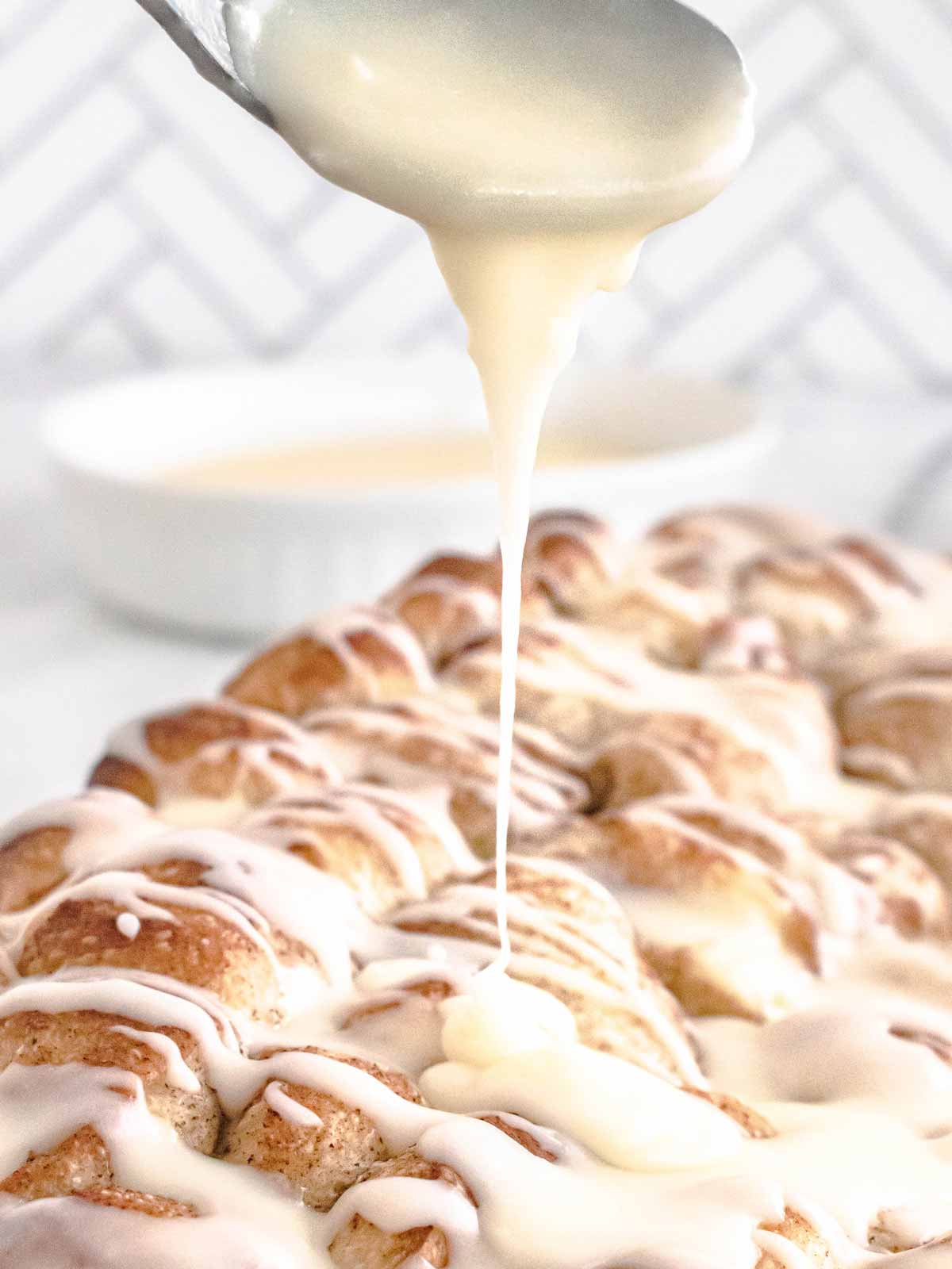 frontal view of cinnamon roll frosting drizzling from spoon over cinnamon roll casserole