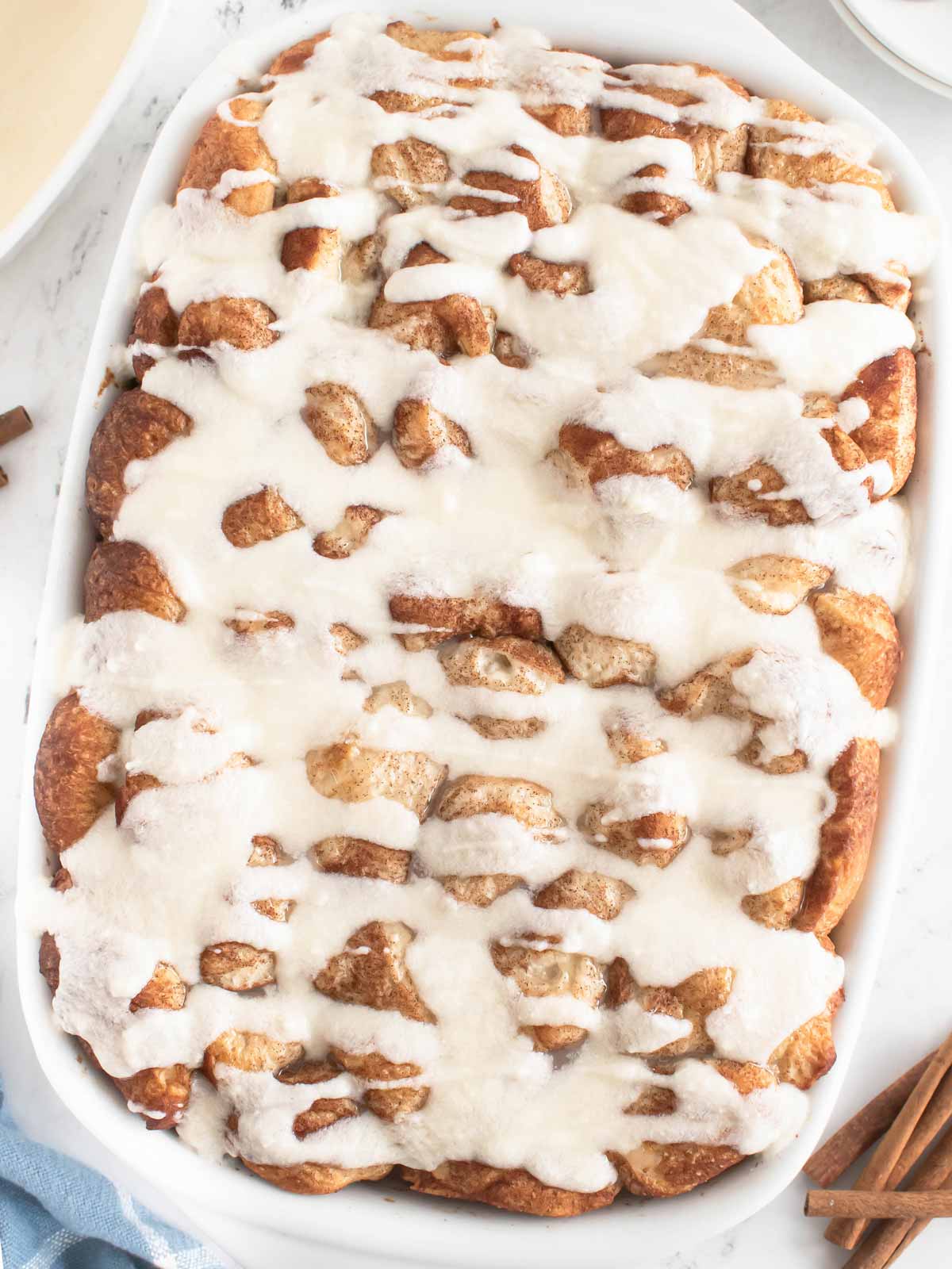 overhead view of baked and frosted cinnamon roll casserole in white casserole dish