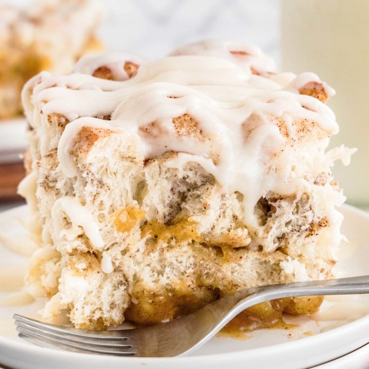 frontal close up view of a slice of cinnamon roll casserole on a white plate with a fork