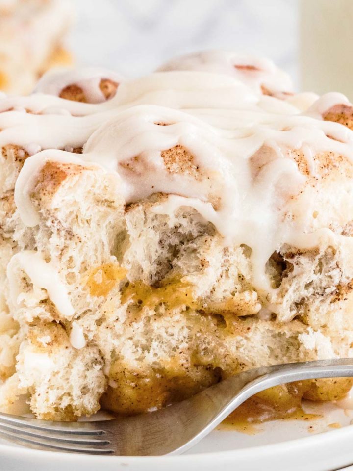 frontal close up view of a slice of cinnamon roll casserole on a white plate with a fork