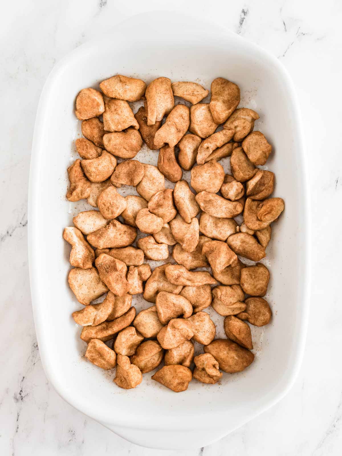 overhead view of frozen bread dough pieces coated in cinnamon sugar mixture in white casserole dish