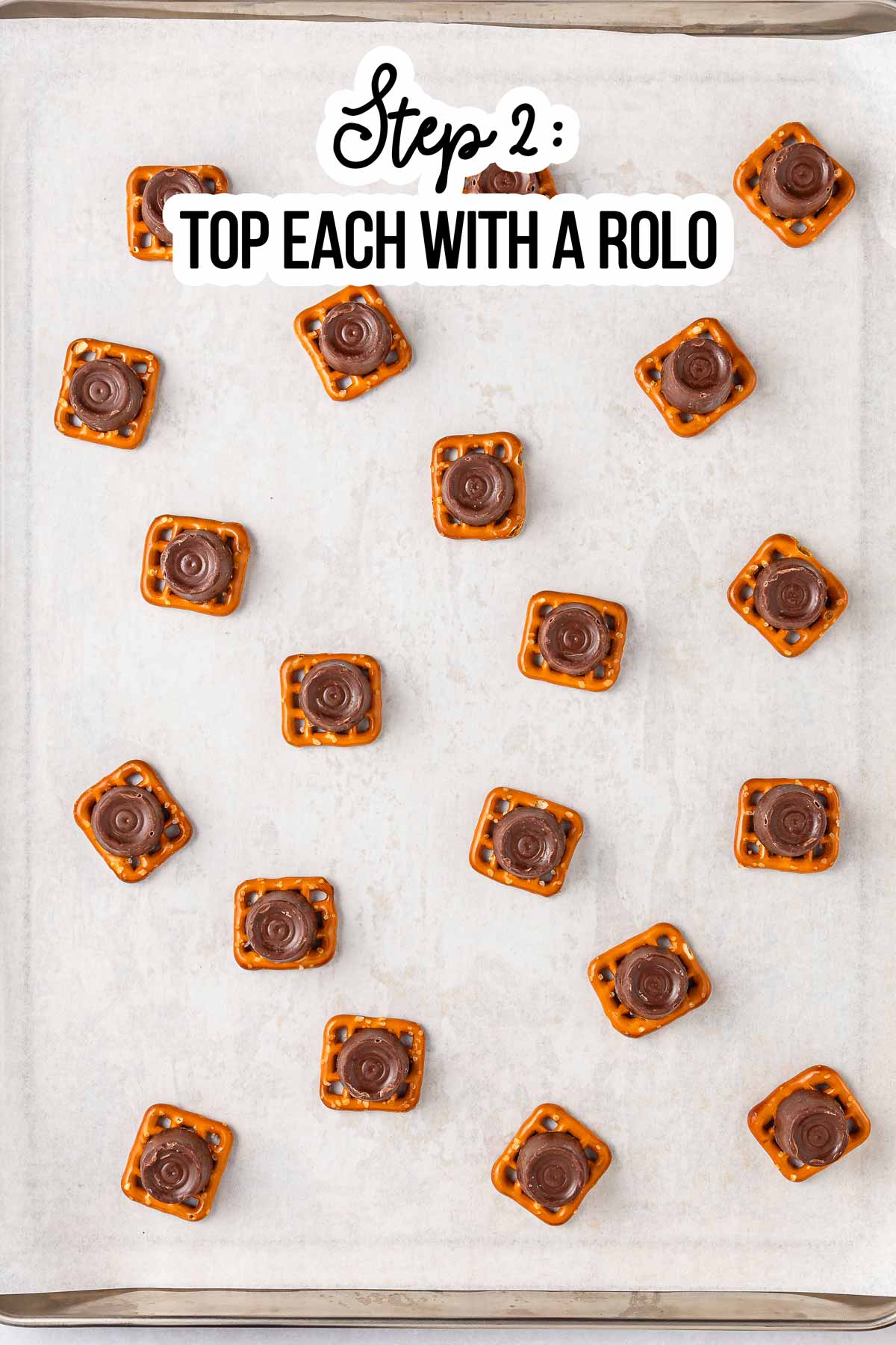 overhead view of pretzel shapes each topped with a chocolate on lined baking parchment